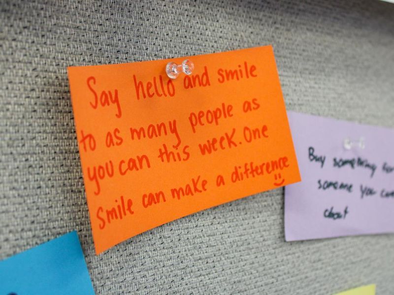 A post it note with a message to be kind is displayed on a bulletin board